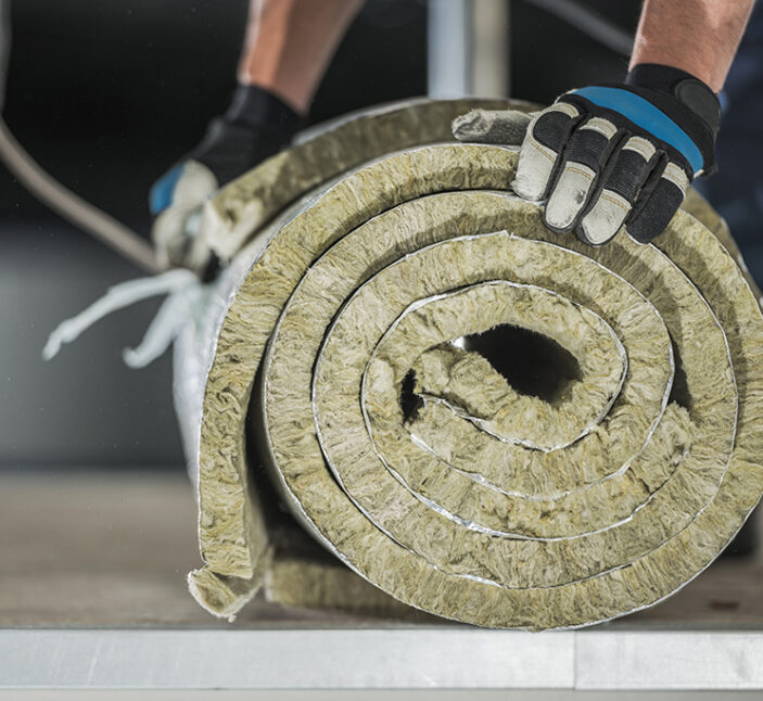 Construction Worker Preparing Roll of Mineral Wool Insulation to Install Inside Warehouse Wall. Thermal Insulation Systems.