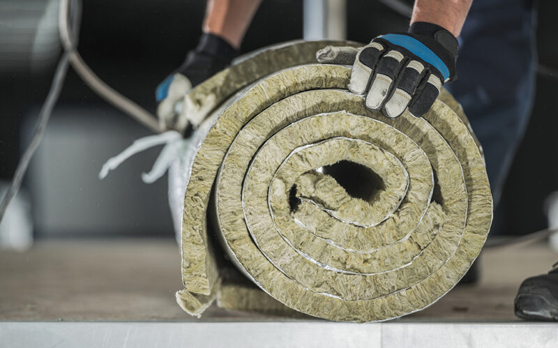 Construction Worker Preparing Roll of Mineral Wool Insulation Construction Worker Preparing Roll of Mineral Wool Insulation to Install Inside Warehouse Wall. Thermal Insulation Systems.